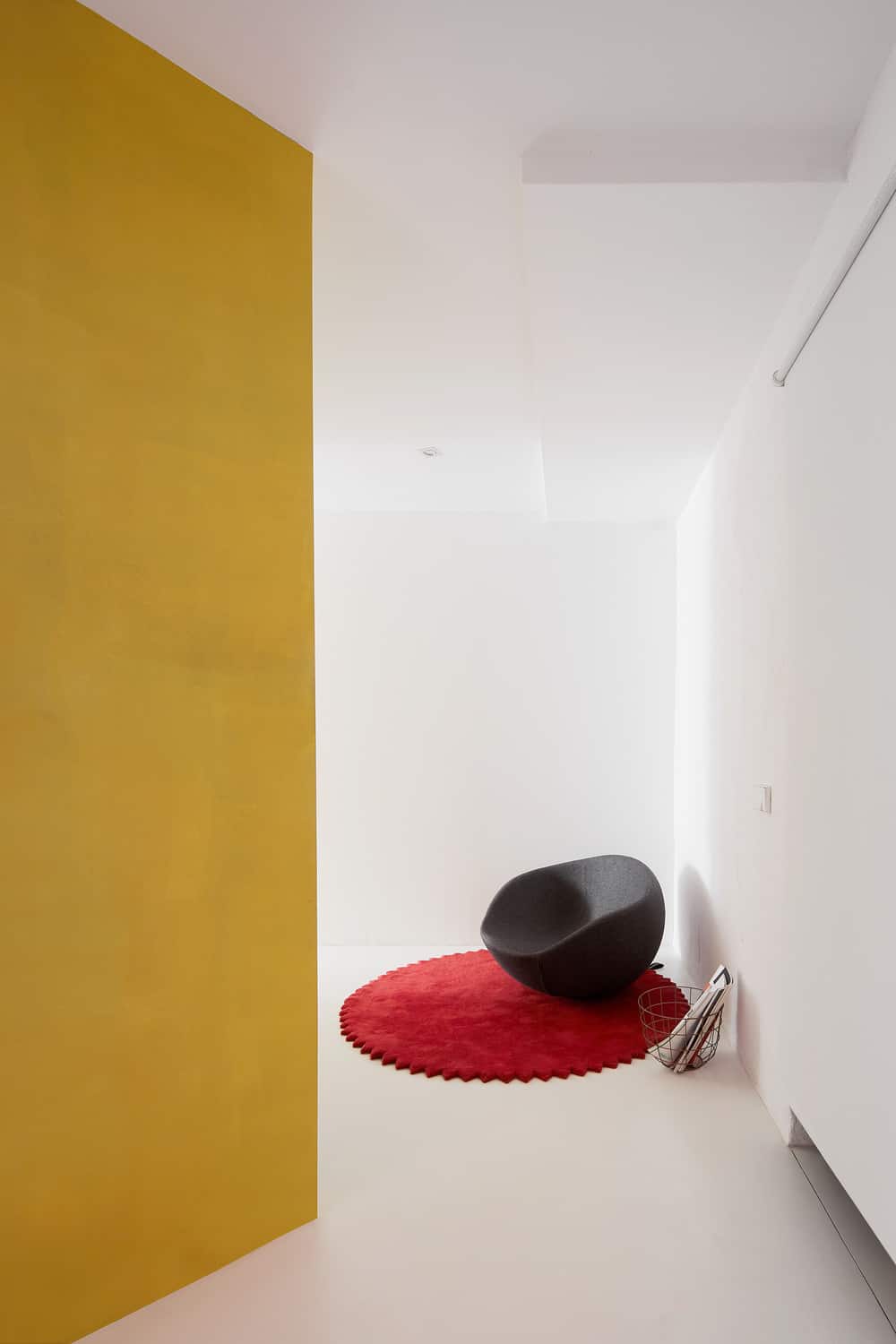 The house has a simple white corner of white walls that make the black chair and red area rug underneath it stand out.