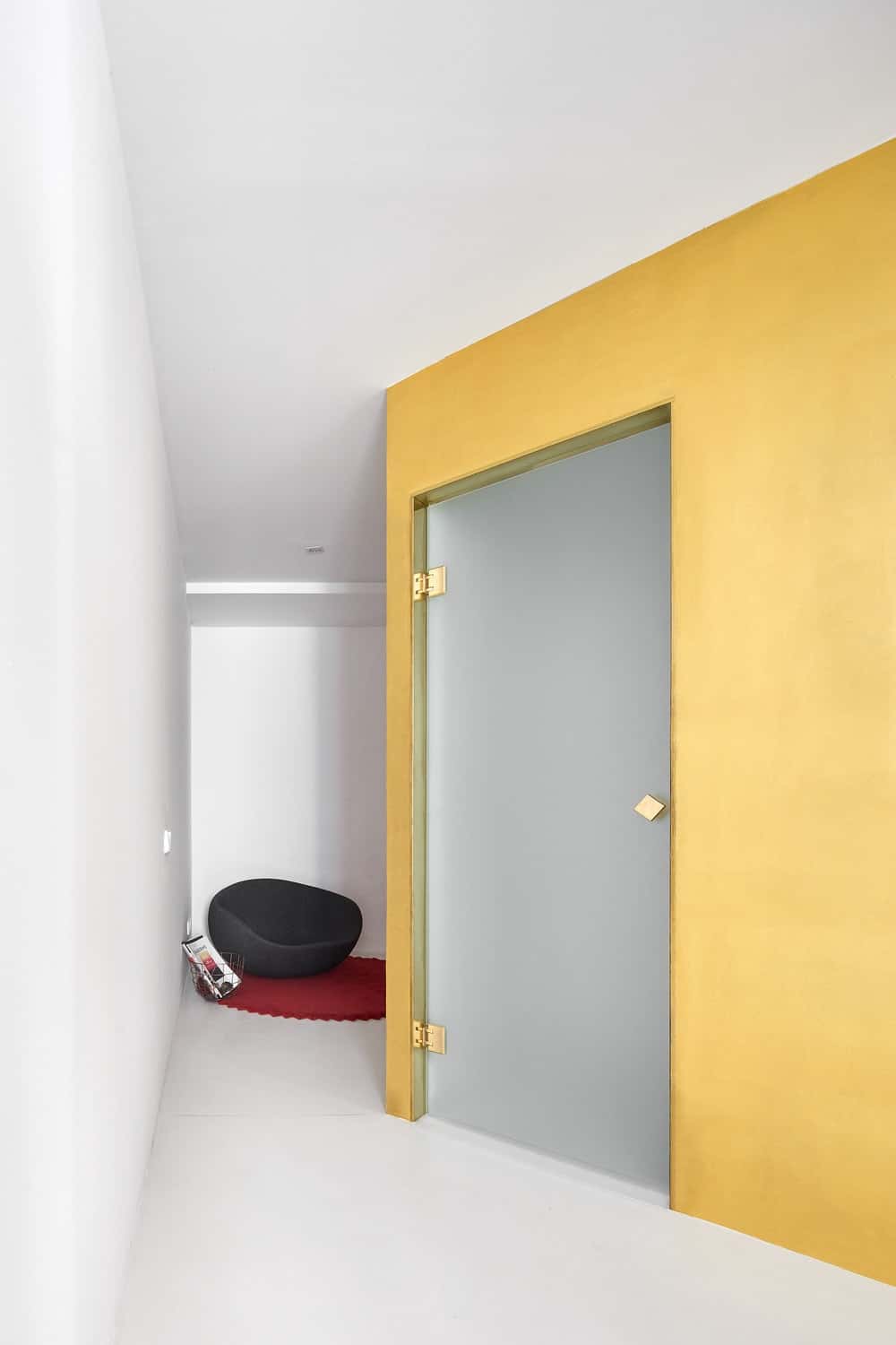 A few steps from the black chair and red area rug is a frosted glass door that contrasts with the yellow walls.