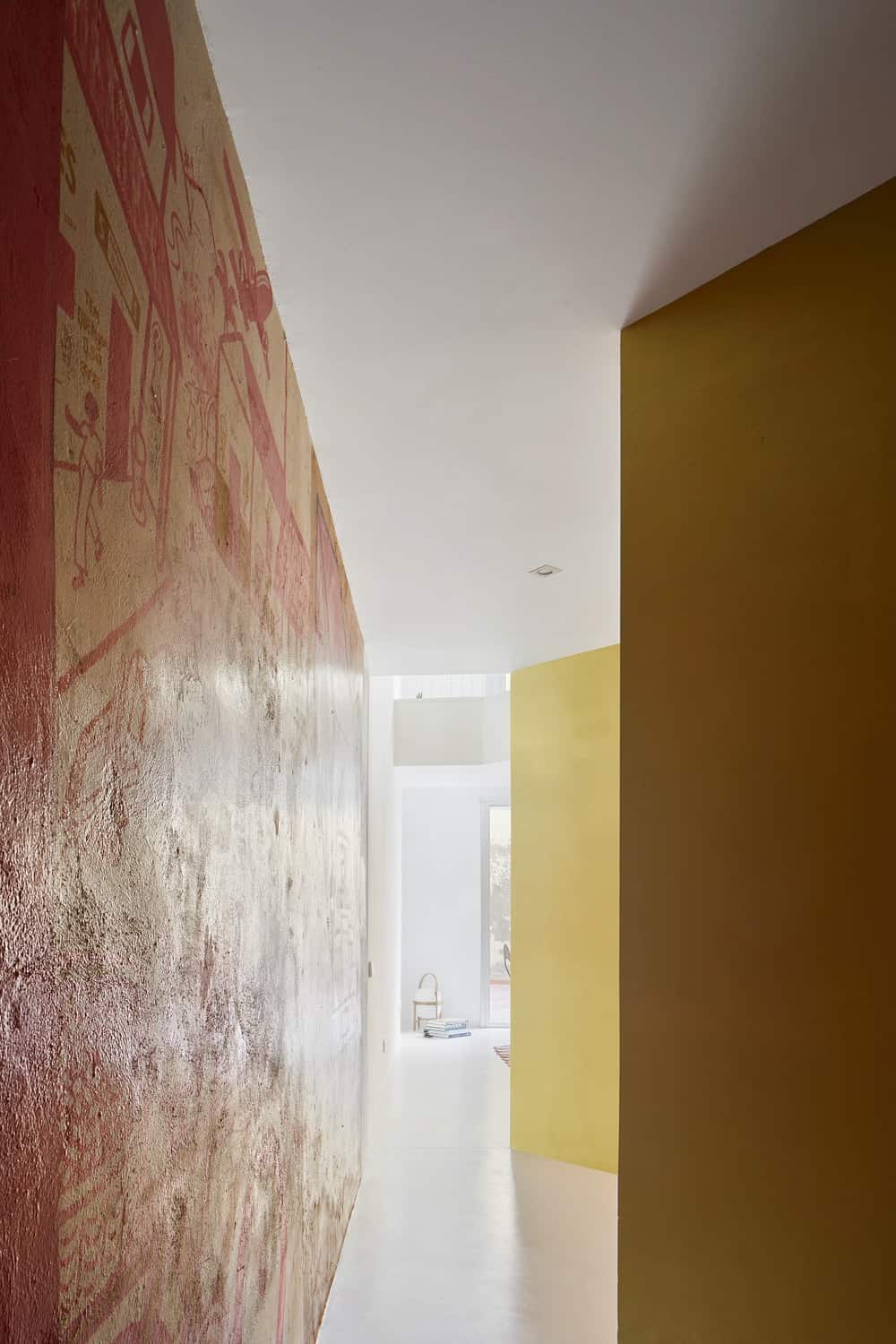 This is the hallway with colorful murals on one side and yellow walls on the opposite side bathed in natural light from the living room in the distance.