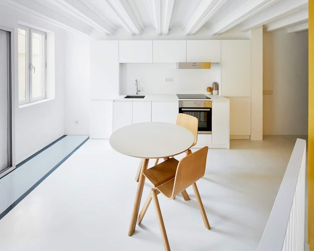 This is a full view of the simple kitchen with its white modern cabinetry, stainless steel appliance and a small dining set across from it.