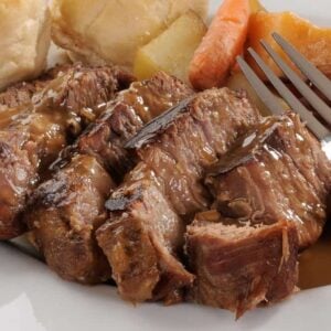 A plate of pot roast and gravy with a side of vegetables and bread.
