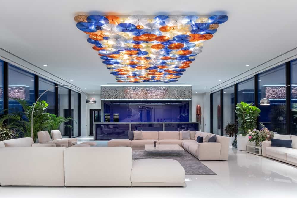 The beige sectional sofas are paired with white coffee tables and the bright blue kitchen structures at the far end.