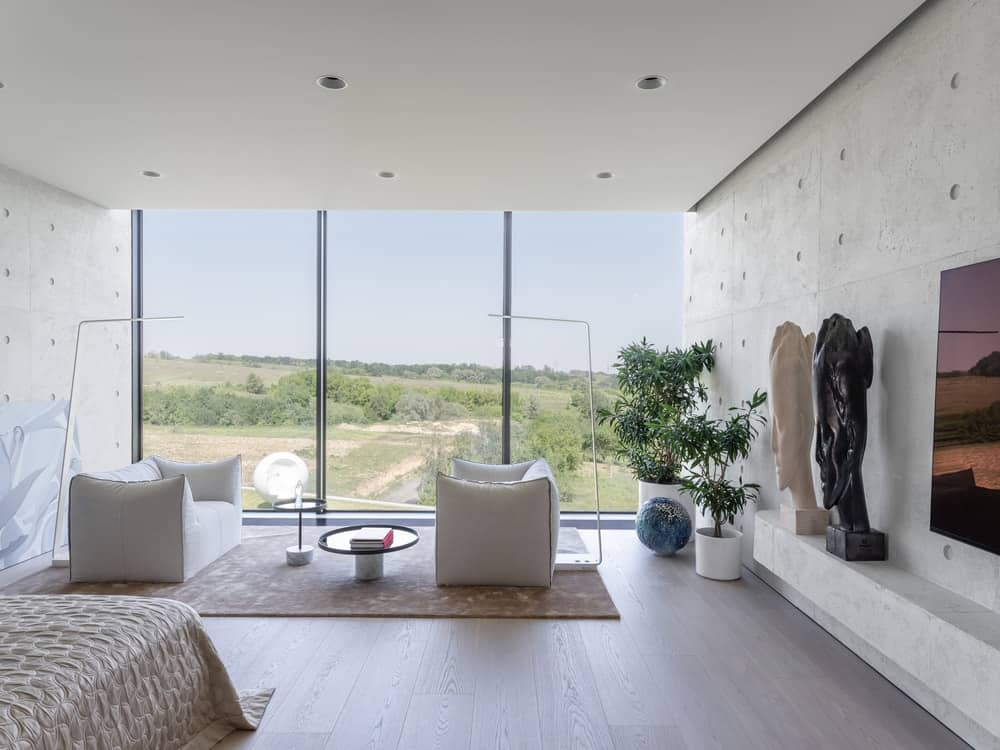 This is a look at the primary bedroom with a sitting area by the large glass wall on the far side opposite the bed.