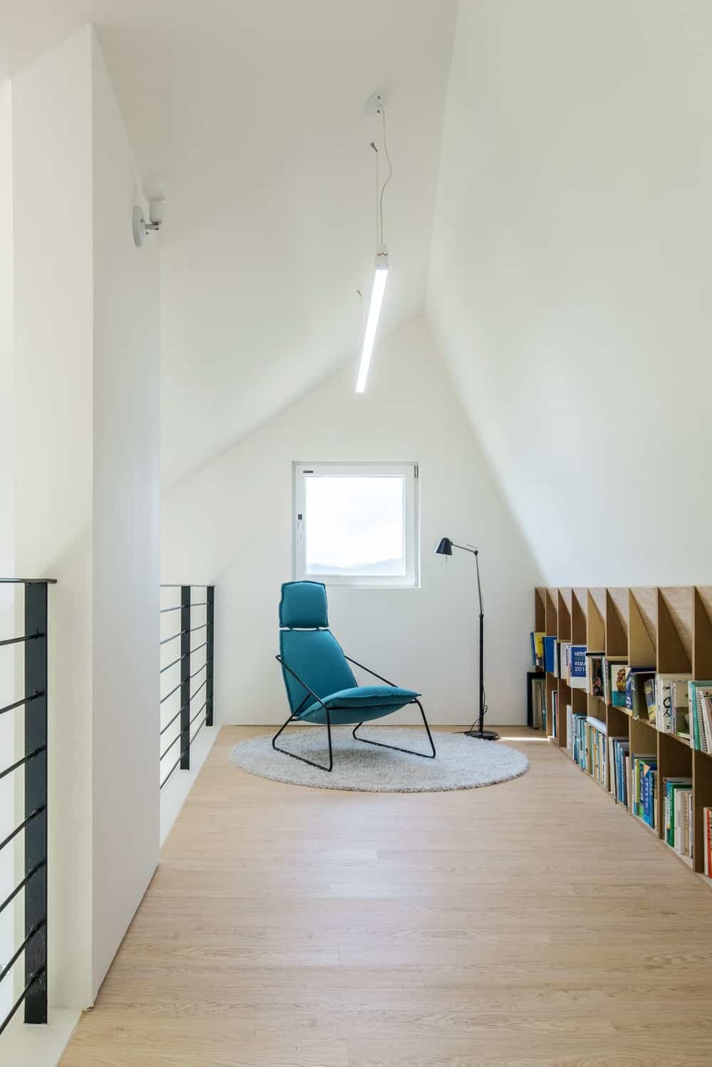 This is a look at the attic library that has a wooden structure built into the wall on the side for books. This is paired with a comfortable chair by the window and lamp.