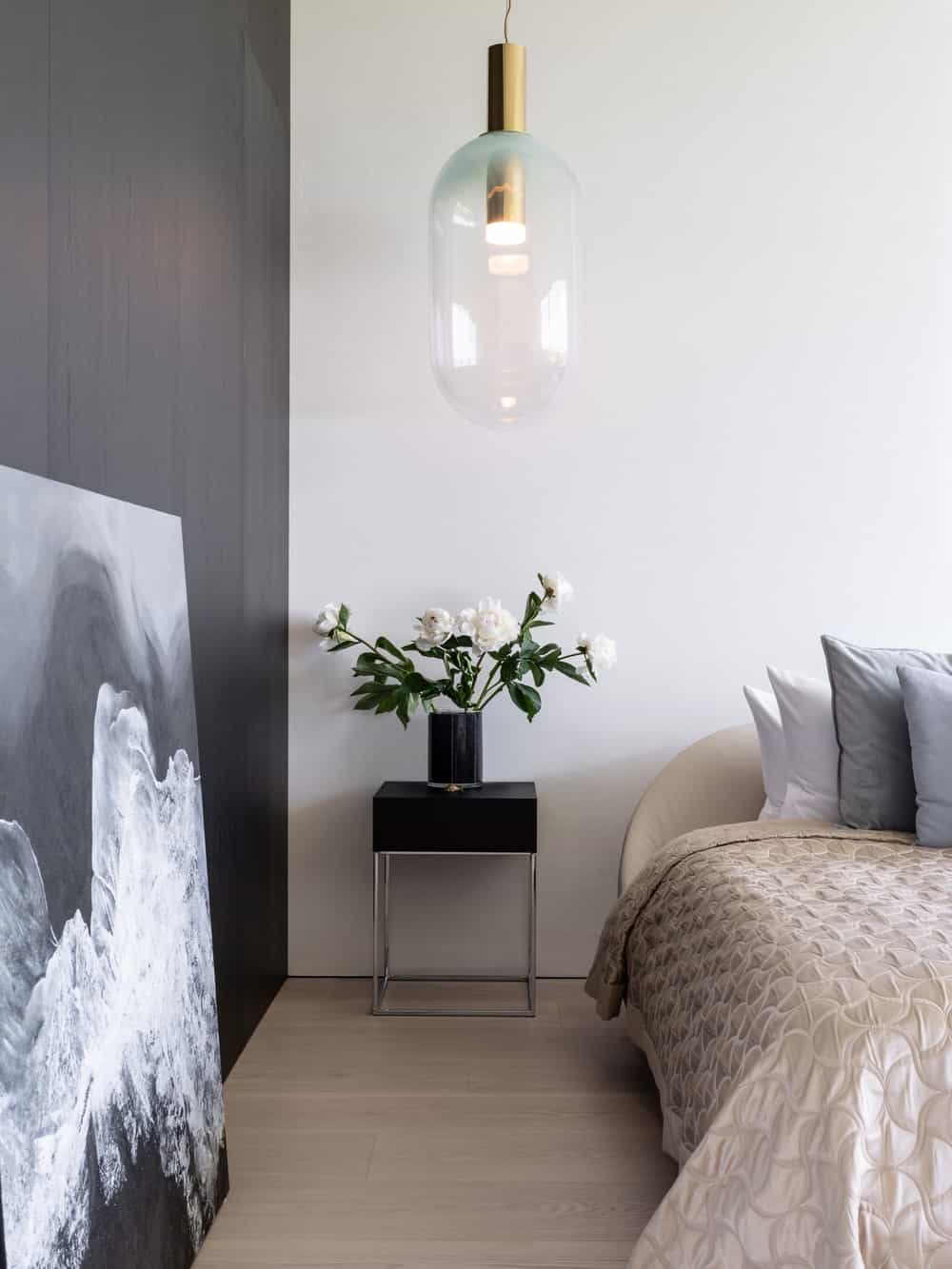 On the side of the bed is a small black bedside table with flower vase.