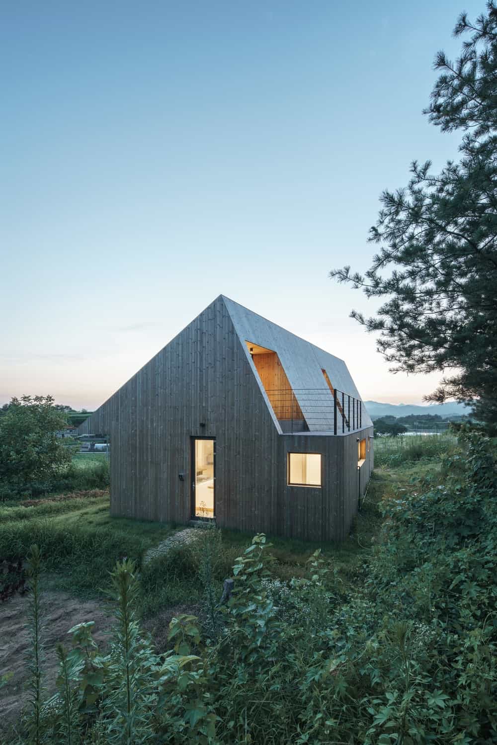 This is a nighttime look at the exterior of the house with multiple large windows that glows warmly from the interior lights.