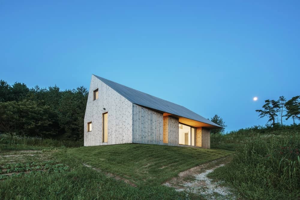 This is a nighttime exterior look at the house with simple patterns and a ceiling over the glass wall of the side.