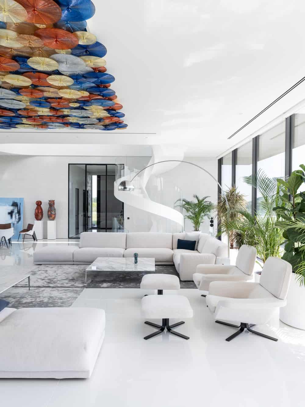 Behind one of the bright beige sectional sofas of the living room is the white spiral staircase by the entryway with glass doors.