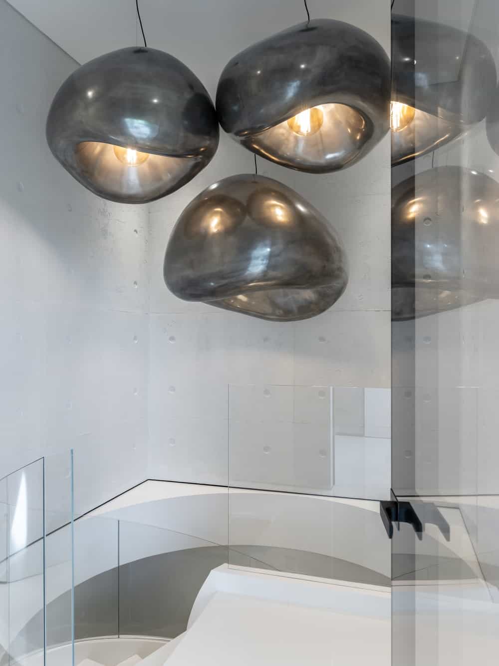 This is a close look at the top of the white spiral staircase topped with a trio of light fixtures that stand out against the bright walls.