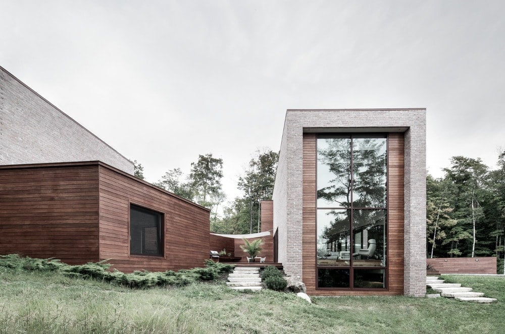 This is a look at the back of the house showcasing an outdoor patio in between two structures and large glass windows and walls.
