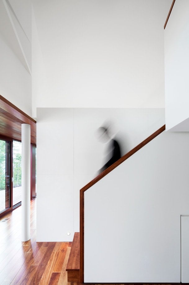 This is a side view of the staircase that has wooden banisters that match the hardwood flooring contrasted by the white walls.