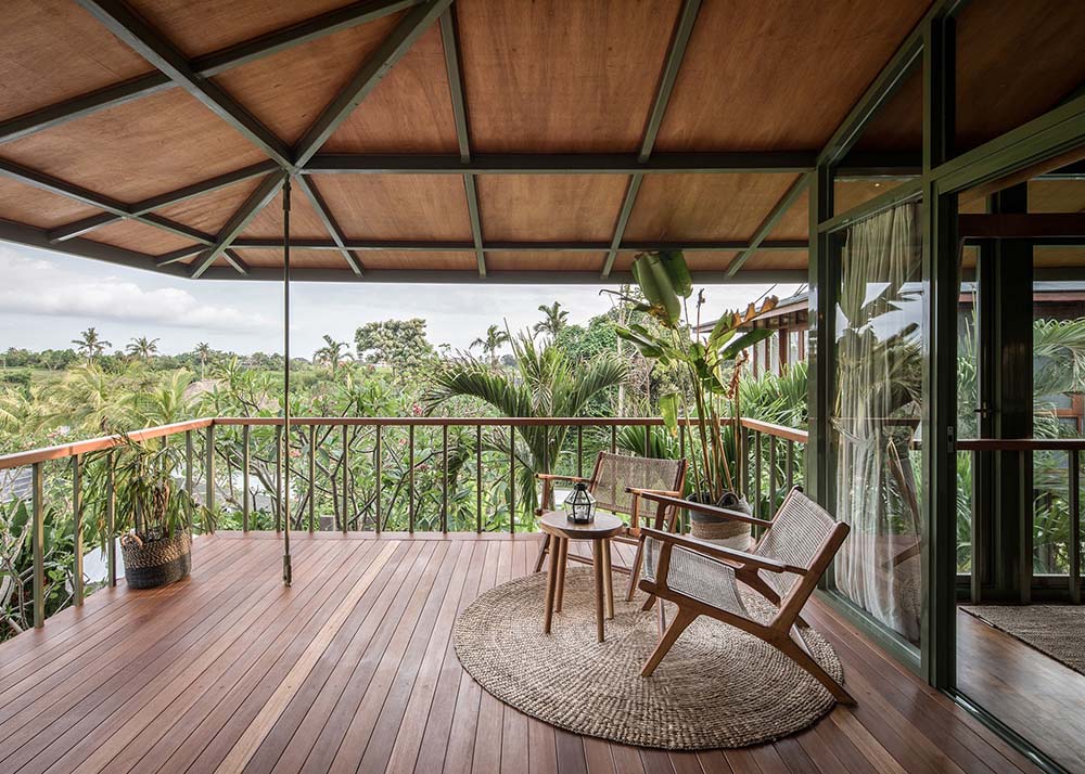 This spacious balcony has a couple of comfortable arm chairs looking at the surrounding foliage of the landscape that is filled with tall trees.