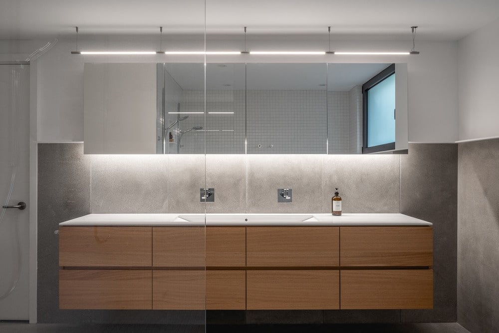 This is a look at the floating wooden vanity of the bathroom topped with a large mirror.
