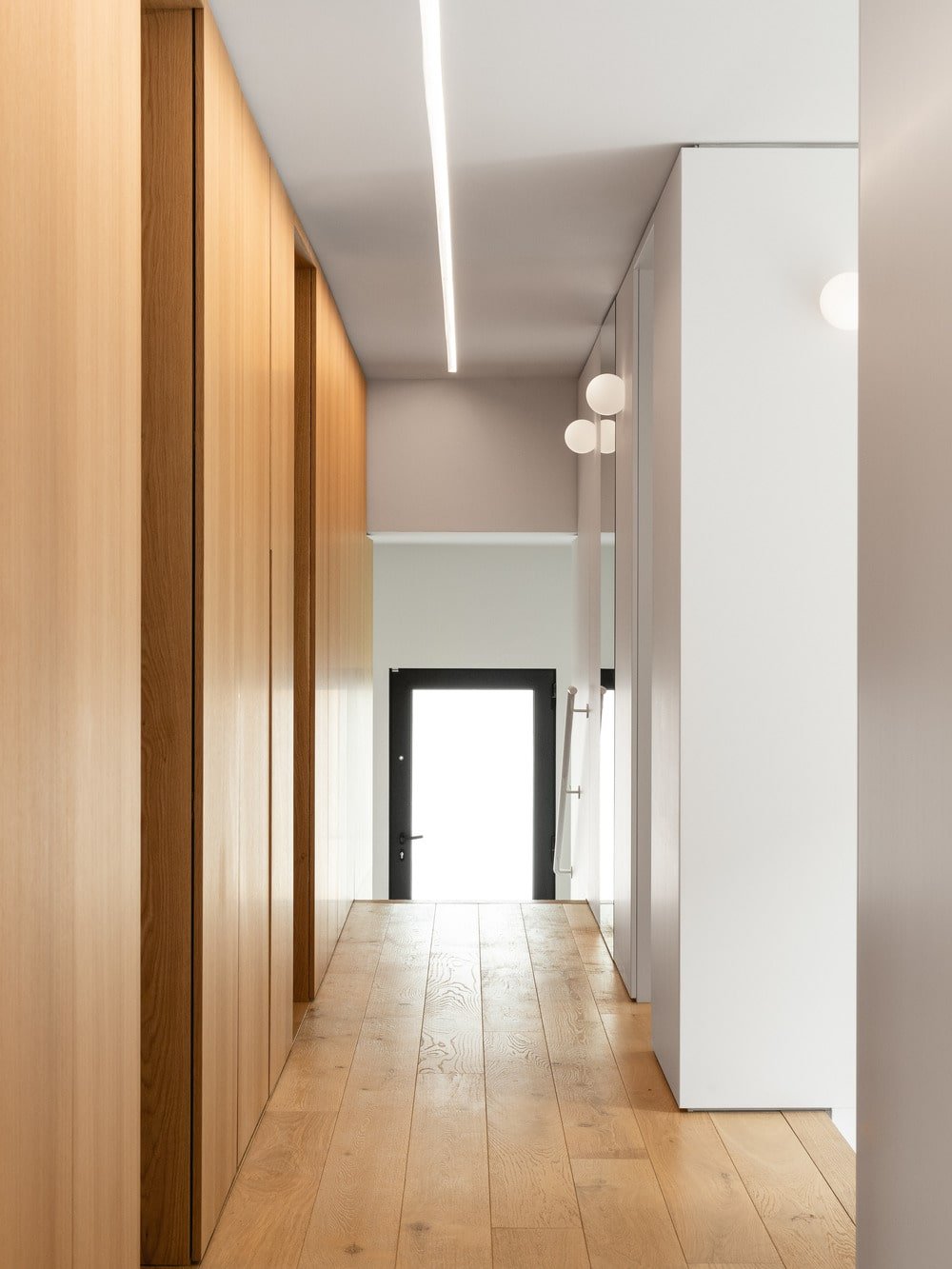 This is a hallway within the house that has wooden walls on the sides brightened by the bright ceiling and pillars.