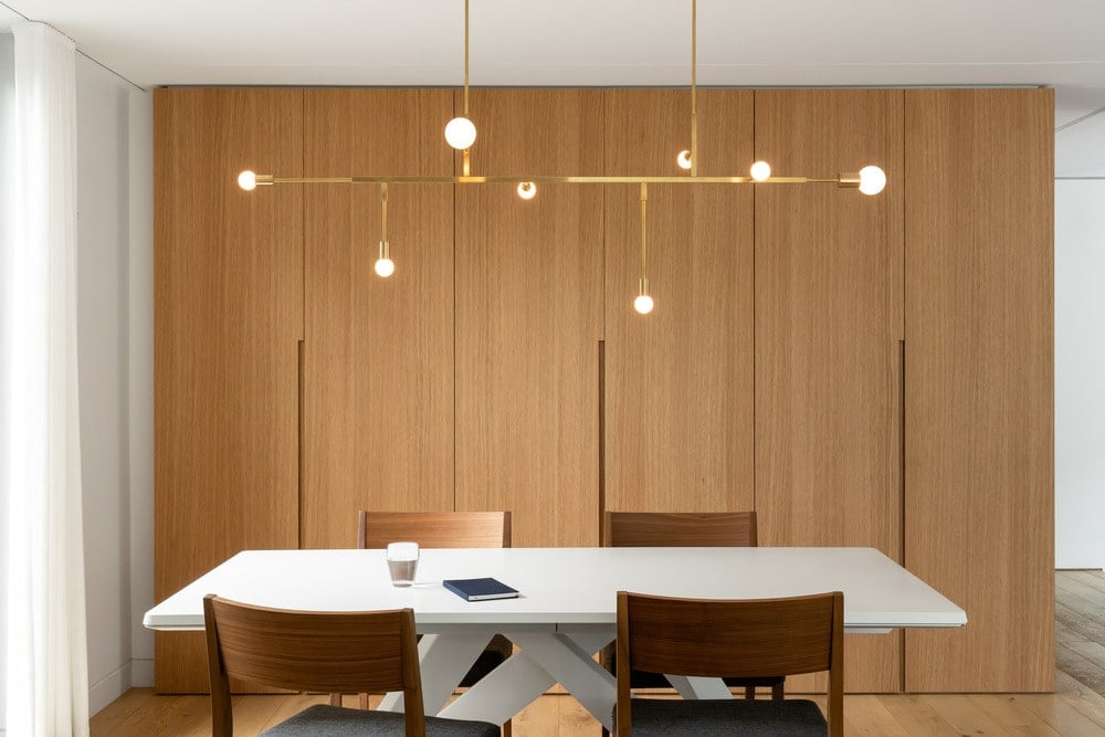 The white dining chair is surrounded by the wooden dining chairs topped with a modern chandelier.