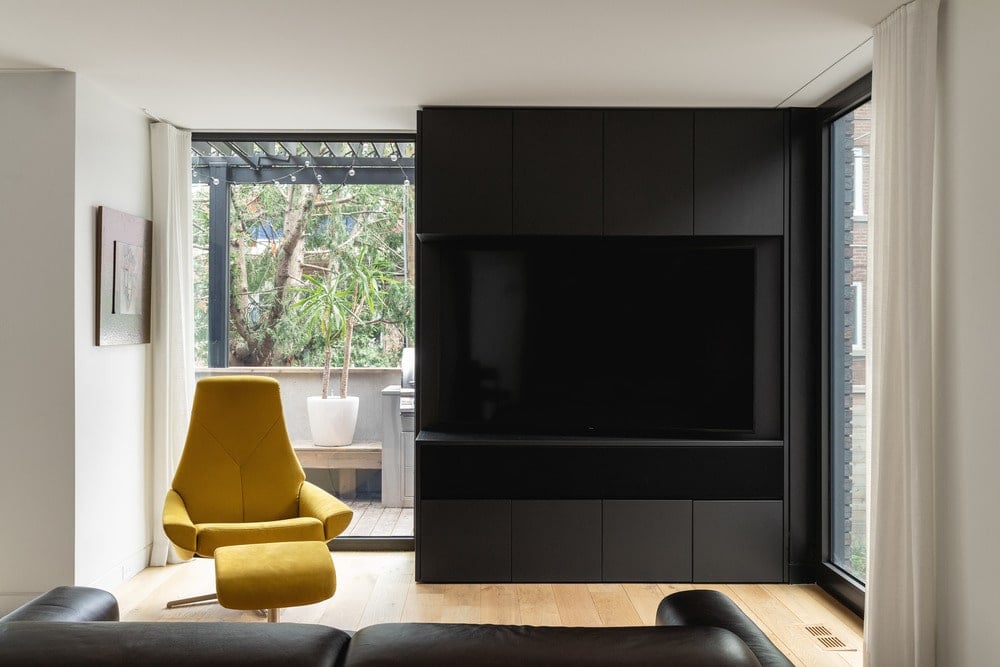 The living room has a large black TV frame across from the black leather sofa that stands out against the light hardwood flooring.