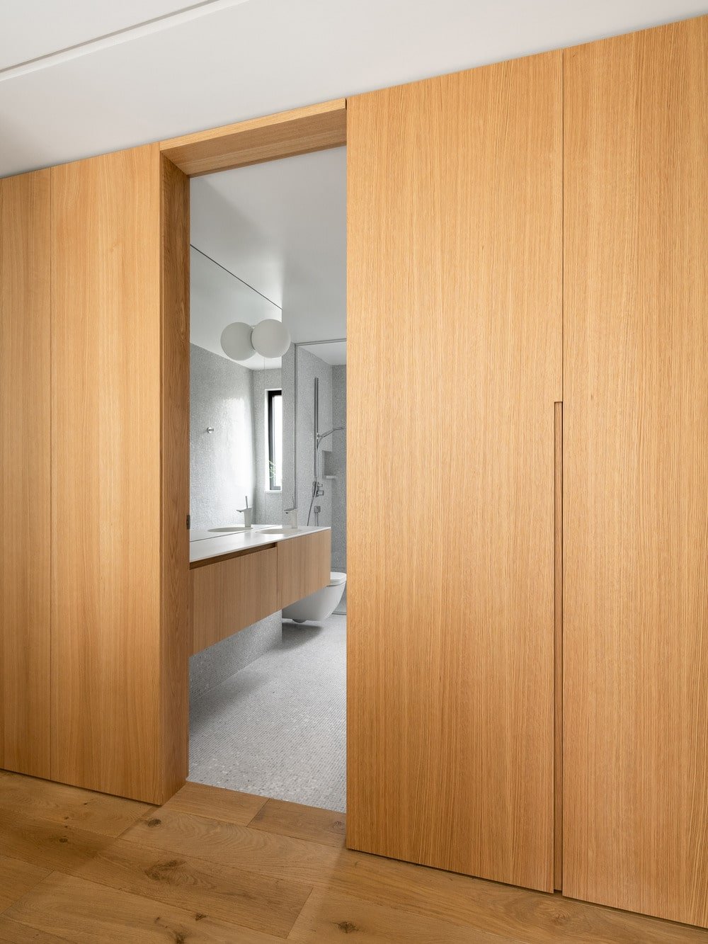 The open door of the bathroom shows the vanity has the same wooden tone as the walls outside.