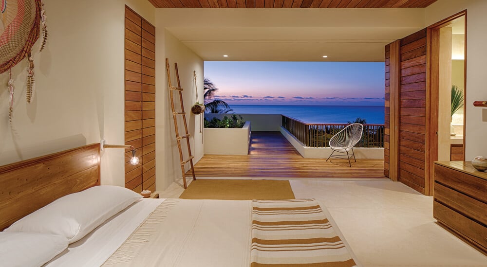 This bedroom has a large bed, a bathroom with a wooden sliding door and a view through the balcony.