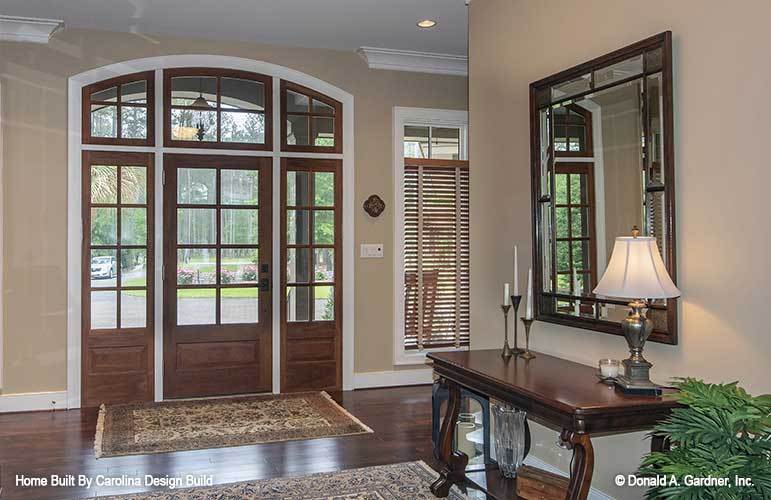 The foyer has a glass framed entry door and a wooden console paired with a decorative mirror.