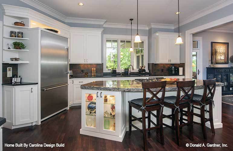 The breakfast island has built-in cabinets, small glass pendants, and cushioned counter chairs.