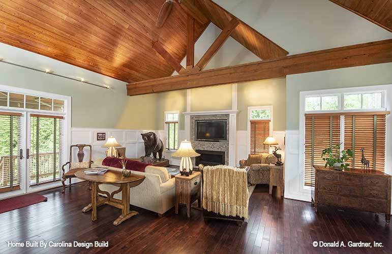 Recreation room with a vaulted ceiling, cozy seats, wooden tables, and a fireplace with a TV on top.
