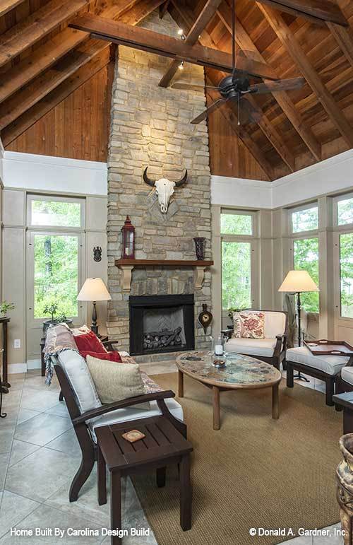 Sunroom with cushioned seats, a stone fireplace, and a cathedral ceiling clad in wood planks.