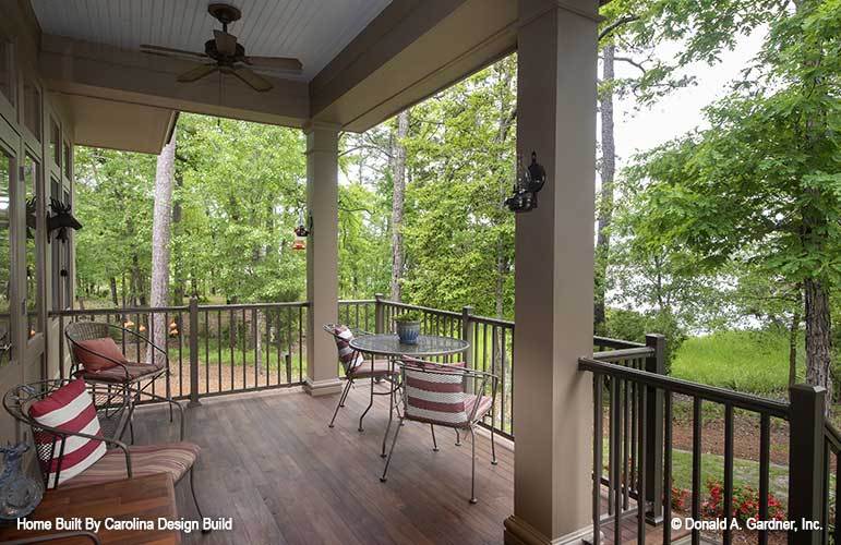 Rear porch with metal chairs, wooden railings, and beige pillars.