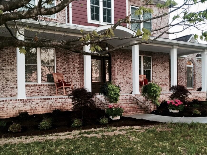 The wide front porch is filled with wooden rocking chairs sitting against the red brick walls.