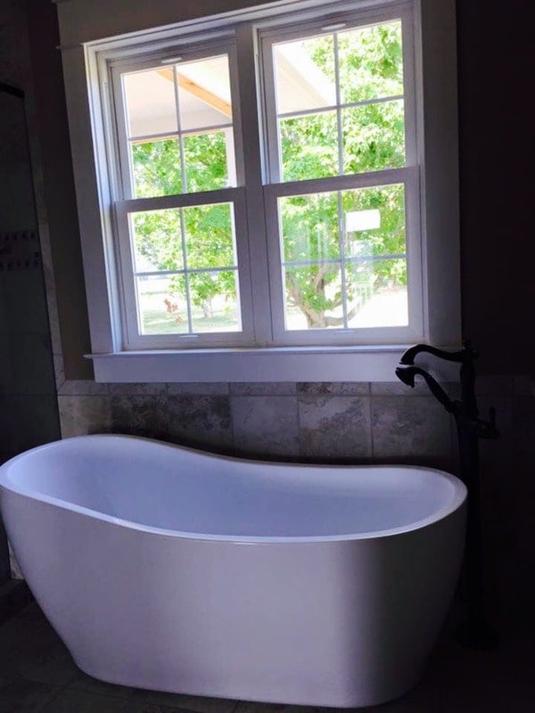 The freestanding tub is placed under the white framed window.