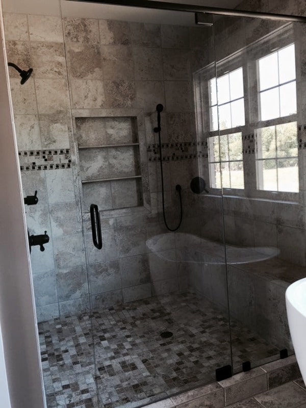 Walk-in shower with inset shelves, wrought iron fixtures, marble tiled walls, and a glass hinged door.Walk-in shower with inset shelves, wrought iron fixtures, marble tiled walls, and a glass hinged door.