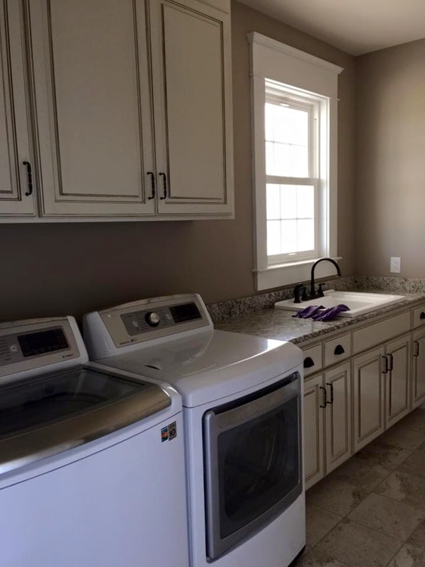 Laundry room with cream cabinetry, white appliances, and a utility sink.