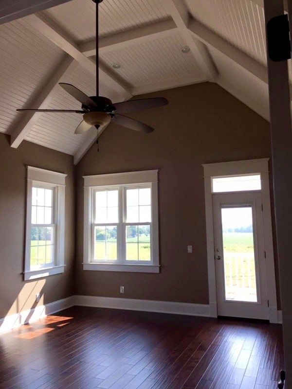 Primary bedroom with a vaulted ceiling, brown walls, wide plank flooring, and private access to a covered porch.