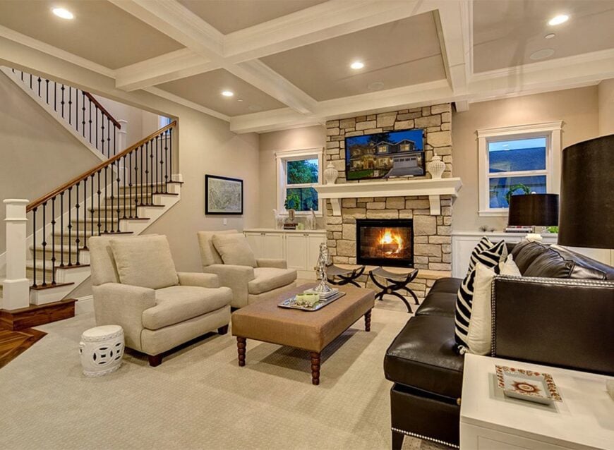 Living room with coffered ceiling, carpet flooring, leather sofa, beige upholstered chairs, and a fireplace.