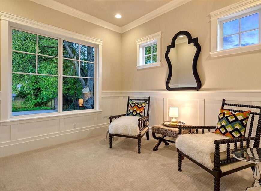 Den with dark wood armchairs and beige walls adorned with white wainscoting and a decorative mirror.