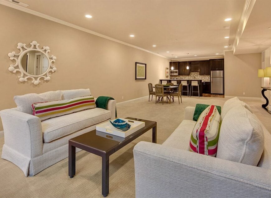 A large recreation room with beige skirted loveseats, a wooden coffee table, and a round mirror.