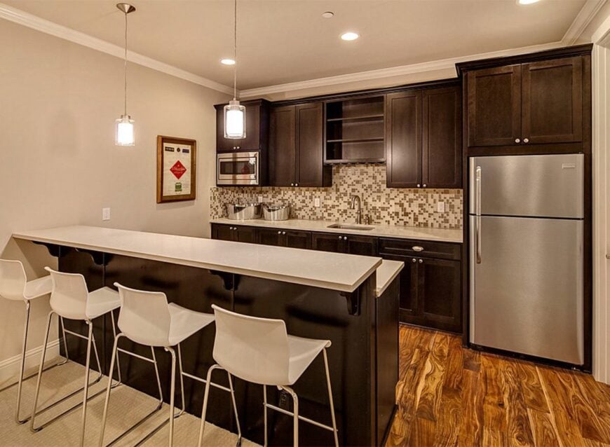 A closer look at the wet bar showing the dark wood cabinetry, stainless steel appliances, and a two-tier island.