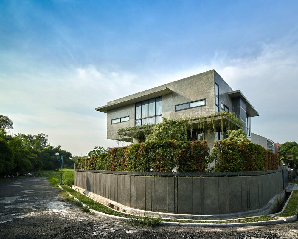 This exterior view of the house showcases its concrete fence wall topped with tall shrub hedges.