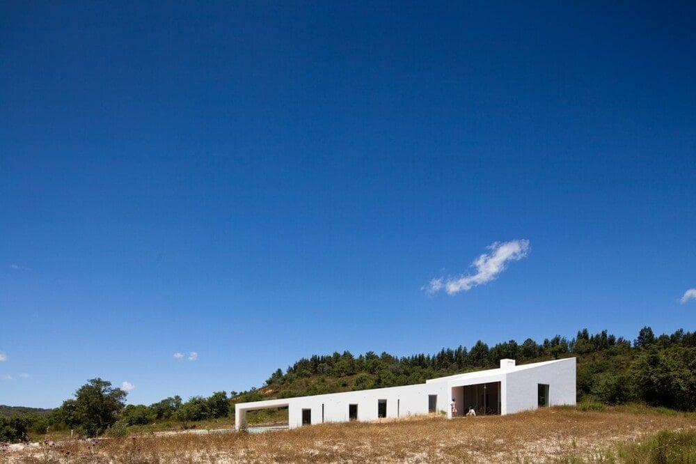 The bright white walls of this adobe house makes it stand out against the surrounding grass and landscape.