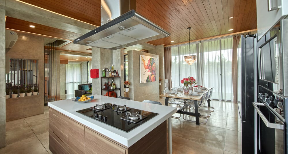 This is a view of the kitchen and the dining area on the far side with a large rectangular dining table by the glass wall.