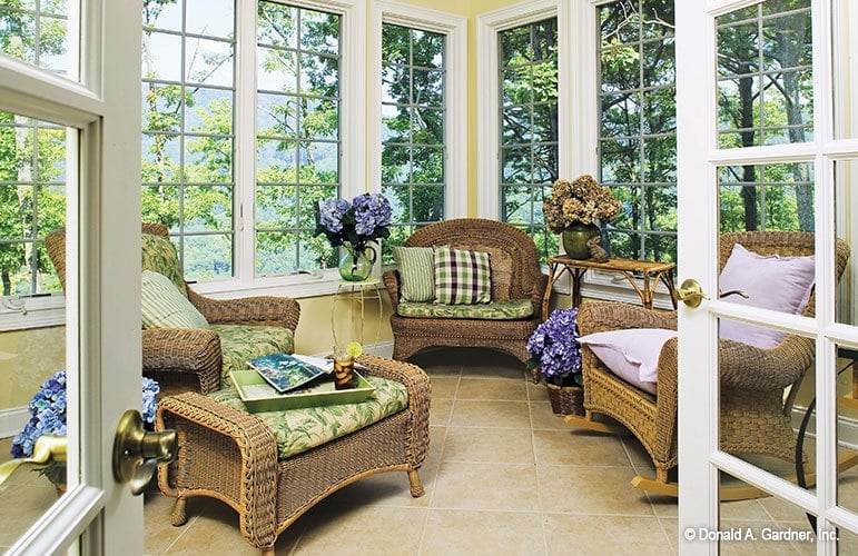 The sunroom is filled with cushioned wicker seats, a wooden side table, and lovely potted flowers.