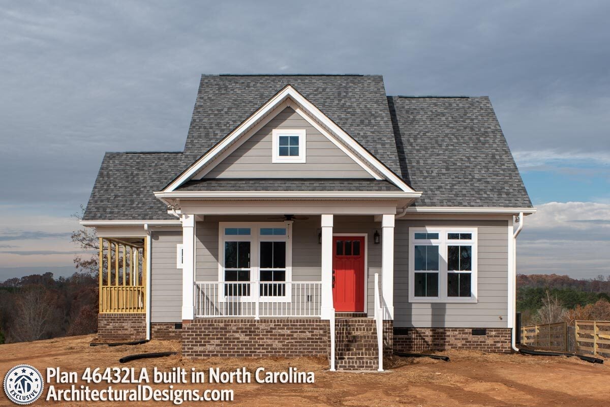 Front exterior view showing the gray siding, brick bases, and a covered entry porch with a red front door.