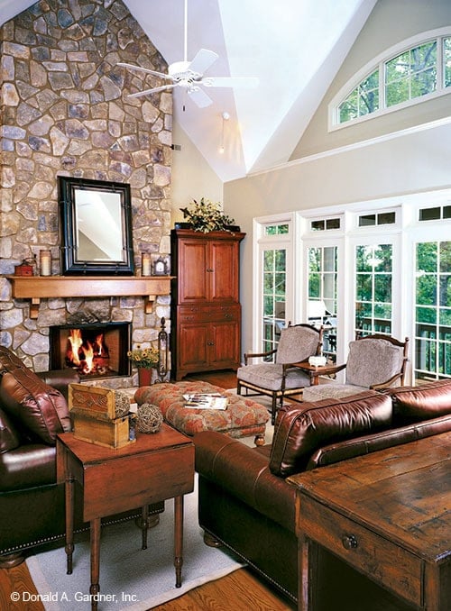 The great room has leather sofas, cushioned seats, a stone fireplace, and massive windows.
