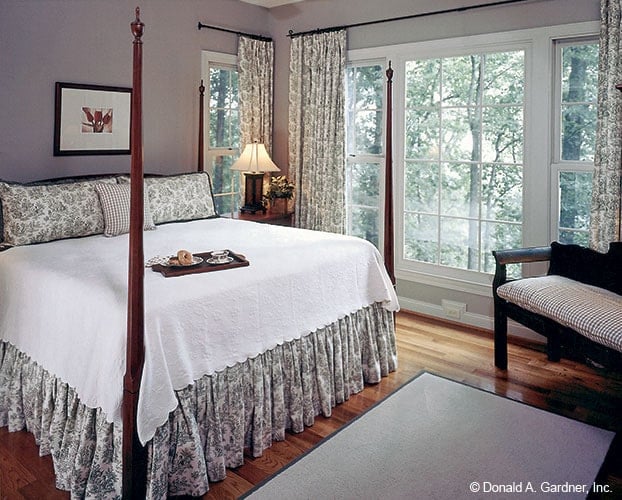 The primary bedroom features a four-poster bed, a sitting area, and white framed windows dressed in patterned drapes.