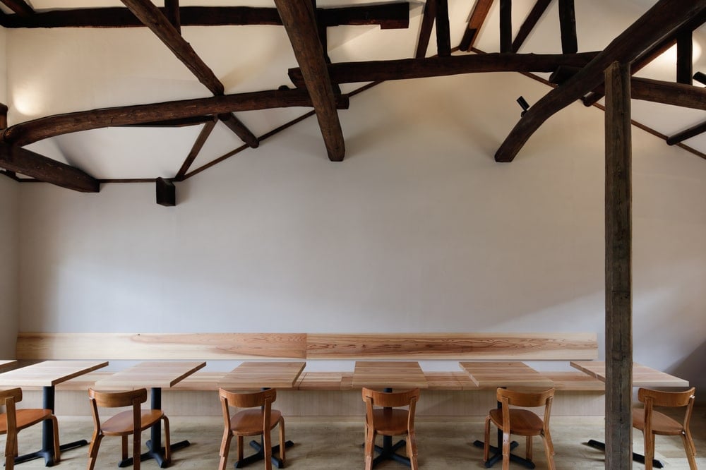 This is a close look at the sets of wooden tables and chairs topped with various rustic exposed dark wooden beams.