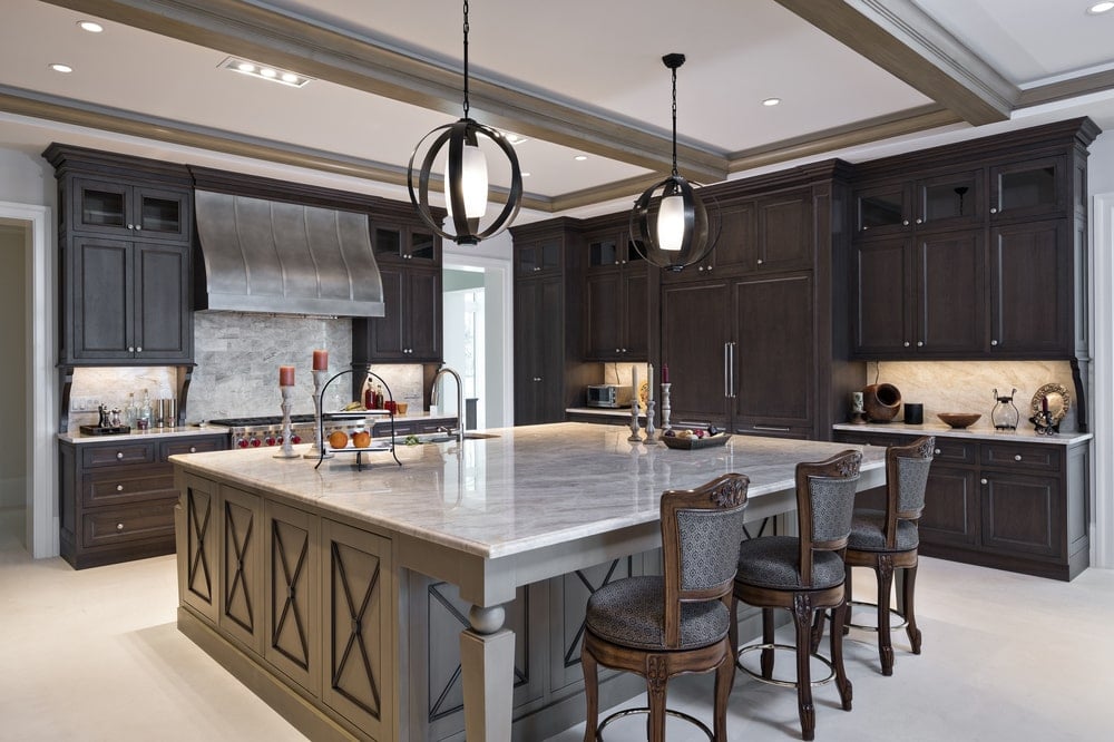 This is a close look at the kitchen that has a large kitchen island in the middle paired with wooden stools and surrounded by dark wooden cabinetry.