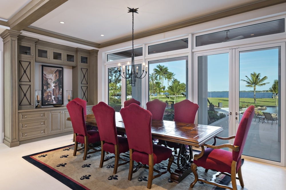This is the formal dining room with red cushioned chairs surrounding a large wooden rectangular dining table topped with a small wrought iron chandelier.