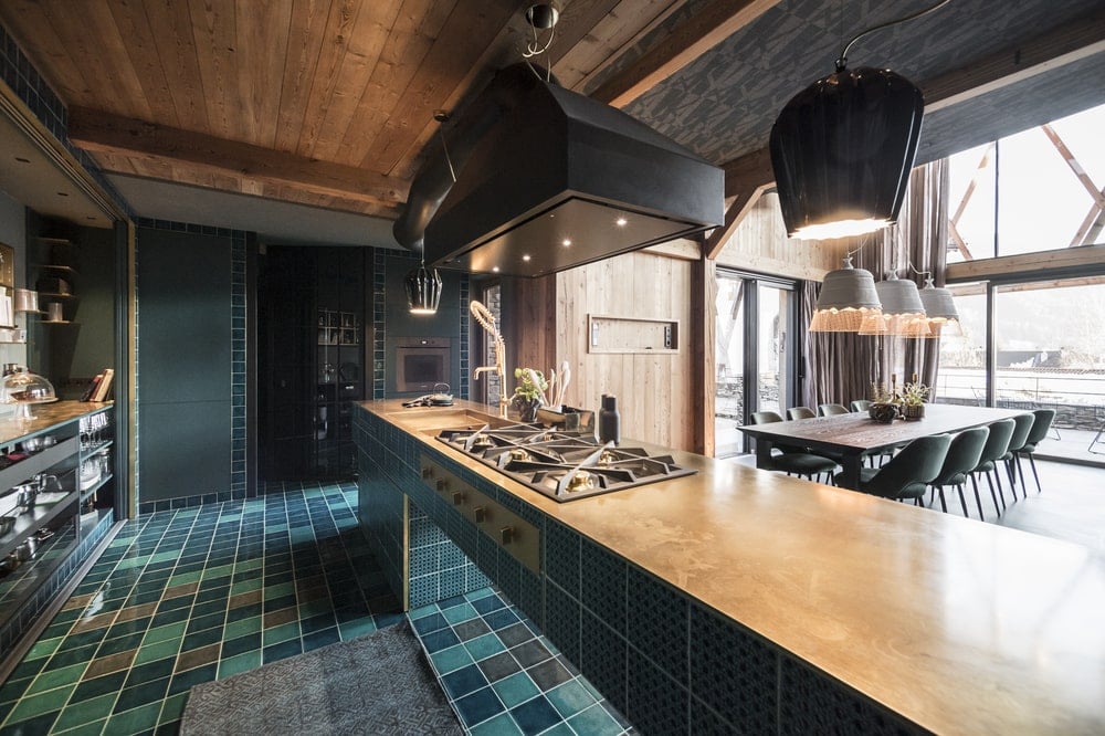 This is a close look at the kicthen peninsula that has a stove top in the middle under a large vent hood with a dark tone.