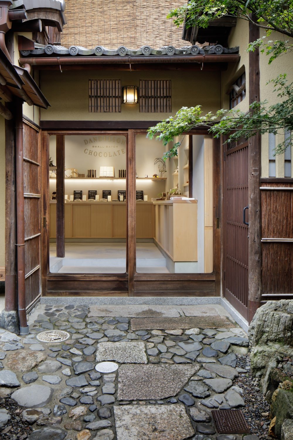 This is a close look at the main entrance that has a wooden frame to its glass doors with additional wooden outer doors and a mosaic stone walkway.