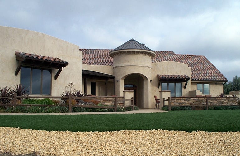 This is a southwestern-style home with adobe exterior walls that has an earthy tone complemented by the terracotta roof tiles and surrounding landscape.