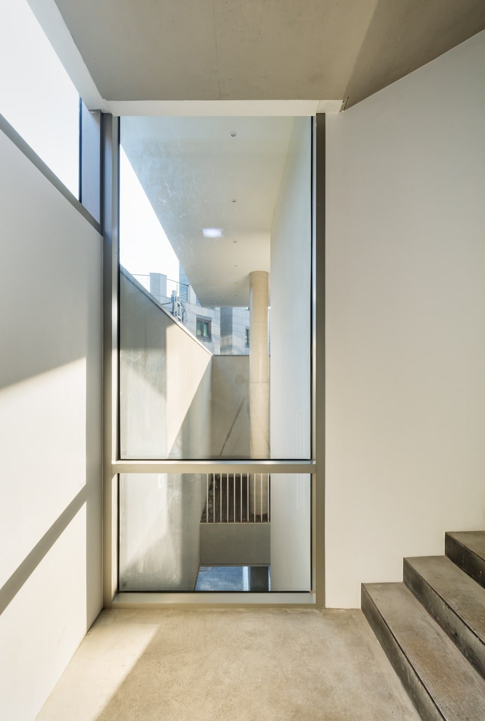 This is a close look at the staircase with beige walls and a large glass window on the corner by the landing for natural lights.